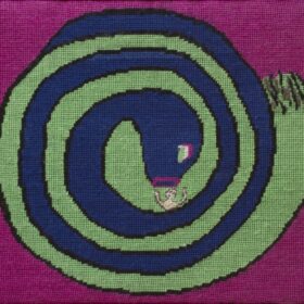 A needlepoint artwork depicting a large, blue and lime green striped snake coiled in a tight spiral on a vibrant magenta background. A small, pale, human-like figure is visible in the snake's jaws near the center.