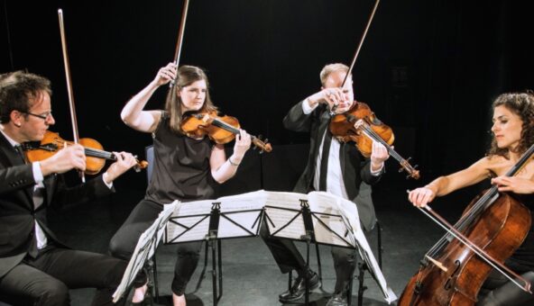 a string quartet dressed in black and playing in front of a black cloth, two have their bows dramatically in the air