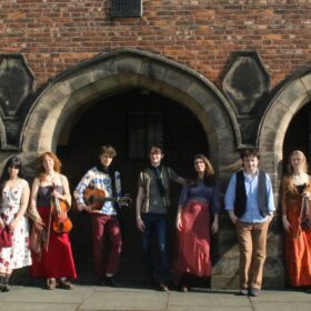 The Manchester Troubadours stood in a line in front of three brick archways on a building.
