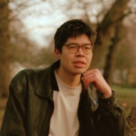 The head and shoulders of writer Will Harris standing outside in a woodland area.