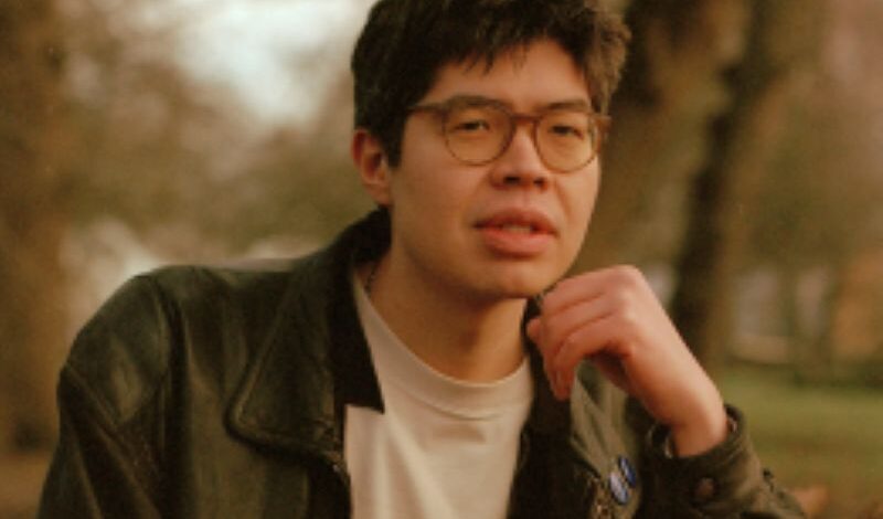 The head and shoulders of writer Will Harris standing outside in a woodland area.