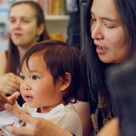 A mother and toddler enjoying a group activity at Z-arts, surrounded by other children and parents in a playful, creative setting.