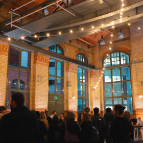 Inside the Engine Hall at the People's History Museum in the evening. There are people stood about and warm white festoon lighting hanging.