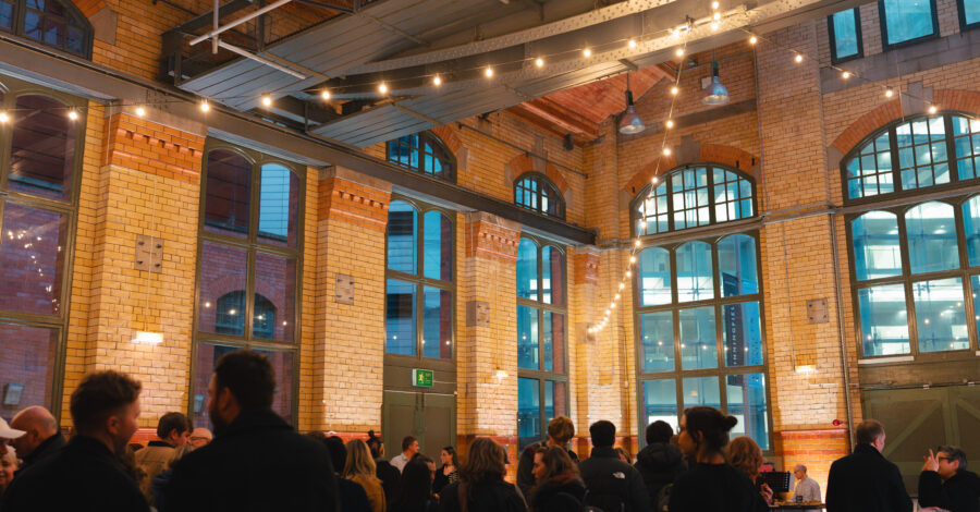 Inside the Engine Hall at the People's History Museum in the evening. There are people stood about and warm white festoon lighting hanging.