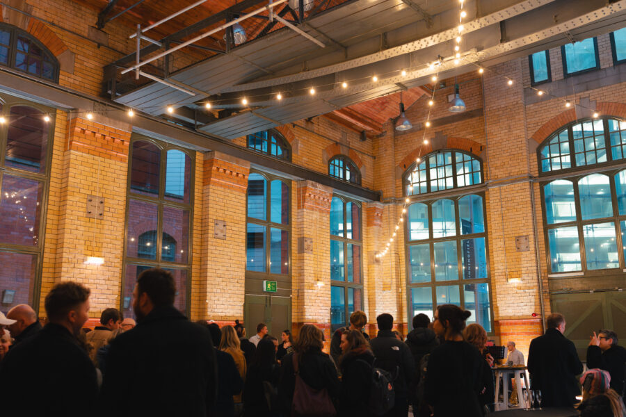 Inside the Engine Hall at the People's History Museum in the evening. There are people stood about and warm white festoon lighting hanging.