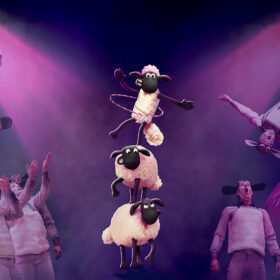 An illustration of three sheep stacked on top of one another on a stage, as performers perform somersaults on each side of them.,