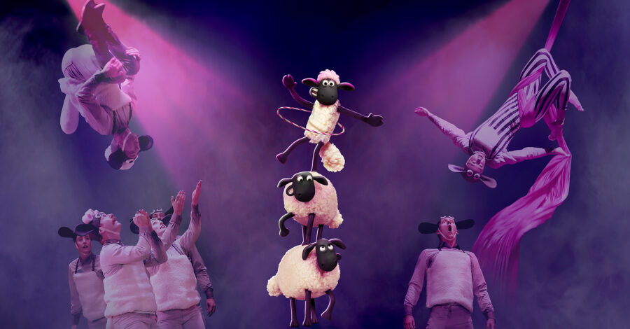 An illustration of three sheep stacked on top of one another on a stage, as performers perform somersaults on each side of them.,