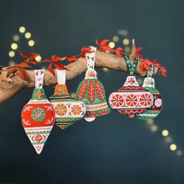 Handcrafted red, green and white fabric Christmas decorations hanging from a branch.