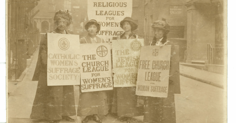 A black and white image of four women holding placards that read 'The Church league of Women's Suffrage', 'Catholic Women's Suffrage Society' and 'Free Church League for Women's Suffrage'.
