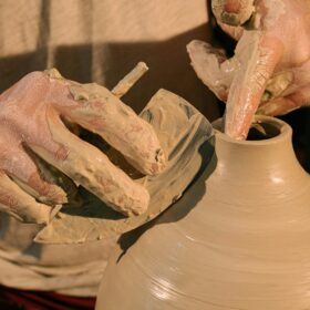 A person making a clay pot on a pottery wheel.