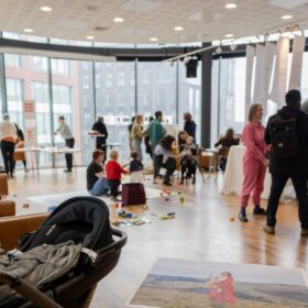 A group of people taking part in a workshop in a large, bright room with big windows.
