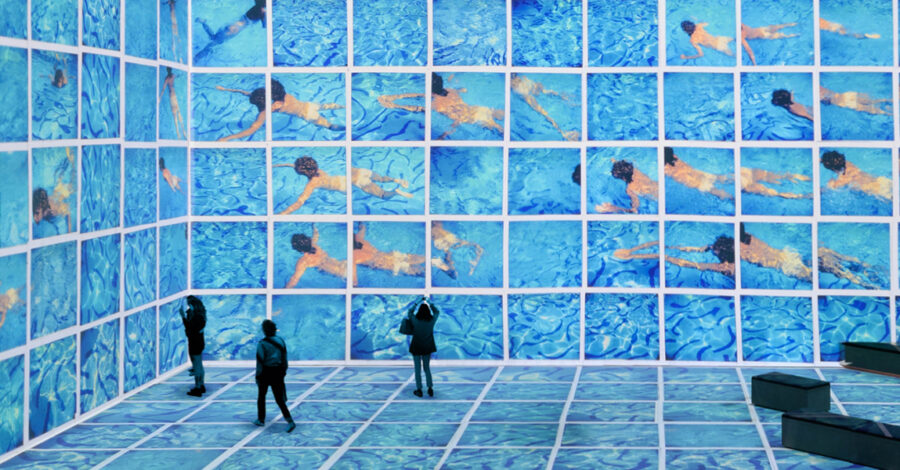 A huge video installation of David Hockney's artwork. It looks like a swimming pool with several people swimming in it and two visitor stand looking at it.