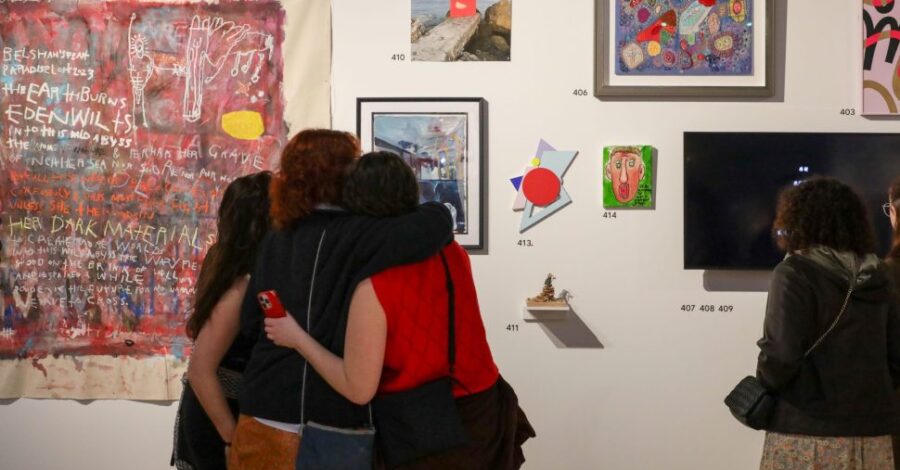 Three people with their arms around each other looking at artwork on a gallery wall.