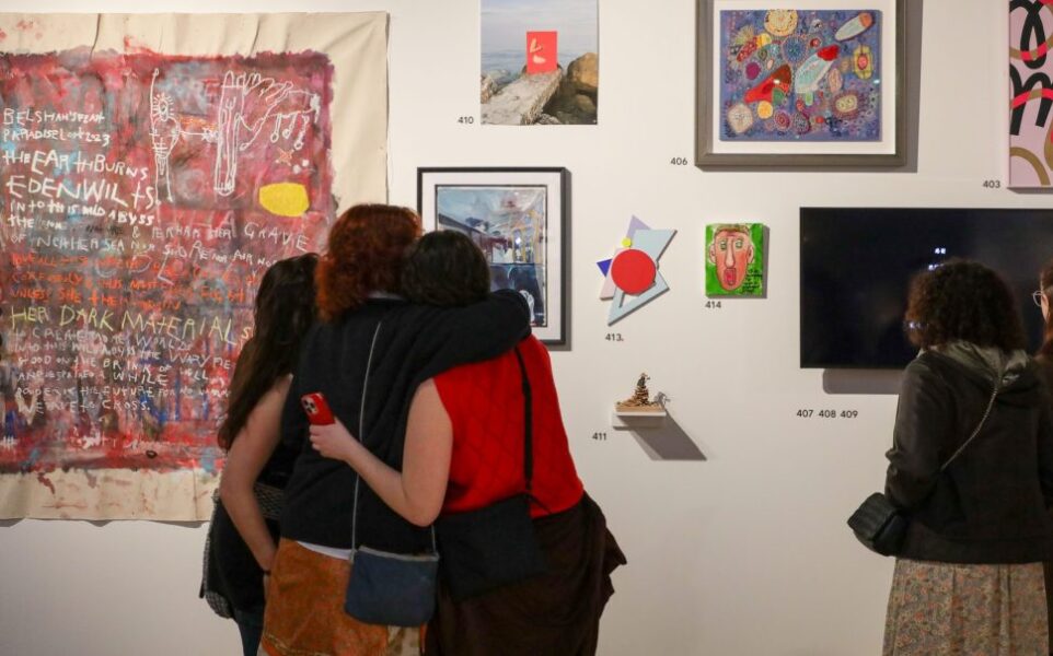Three people with their arms around each other looking at artwork on a gallery wall.