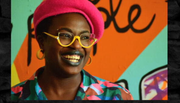 Artist Jasmin Issaka is smiling, and wears a red hat, yellow-framed glasses and a brightly coloured shirt.