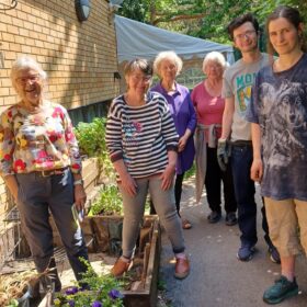 A group of people standing outside in a community garden on a sunny day.