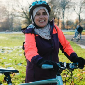 Naz standing with a bike, wearing a hijab and a cycle helmet.