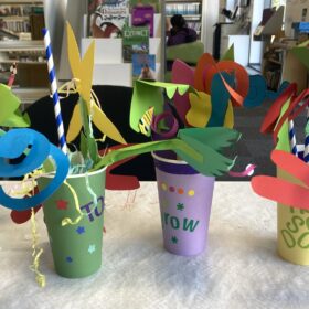 Four artworks made from coloured paper. They are small plantpots made from different coloured paper, each containing a brightly coloured plant, also crafted from paper.