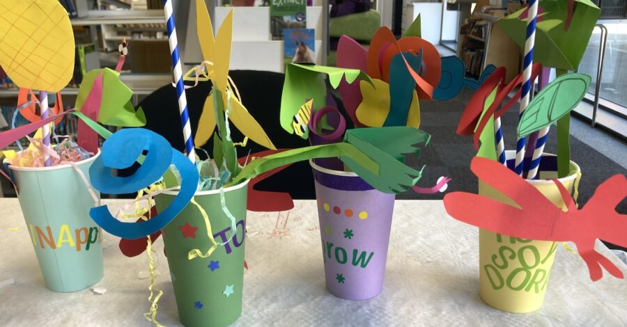Four artworks made from coloured paper. They are small plantpots made from different coloured paper, each containing a brightly coloured plant, also crafted from paper.