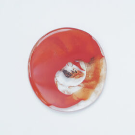 An glass artwork that is glossy and circular in shape and uses the colours red, orange and white.
