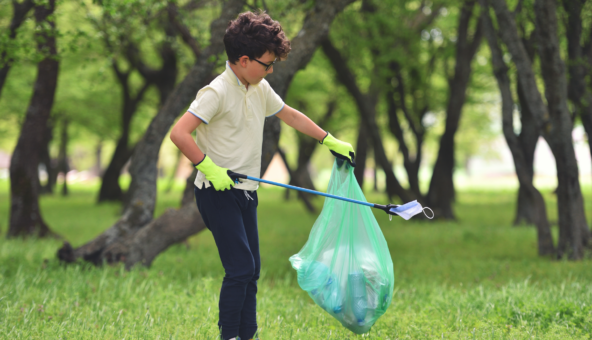 A child holding a litter picker and a green plastic bag as he moves through a park.