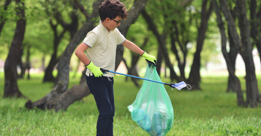 A child holding a litter picker and a green plastic bag as he moves through a park.