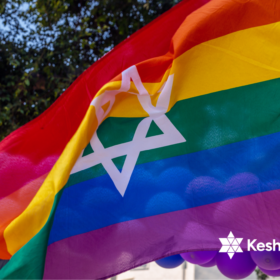 A rainbow coloured flag is waving in the wind. The flag has a white Star of David in the middle. In the bottom right corner we can also see a white logo of KeshetUK.