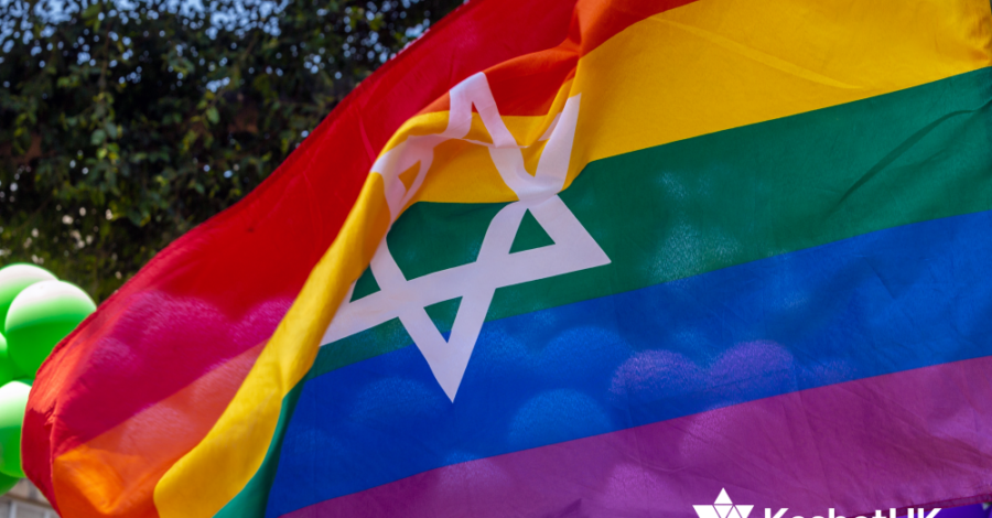 A rainbow coloured flag is waving in the wind. The flag has a white Star of David in the middle. In the bottom right corner we can also see a white logo of KeshetUK.