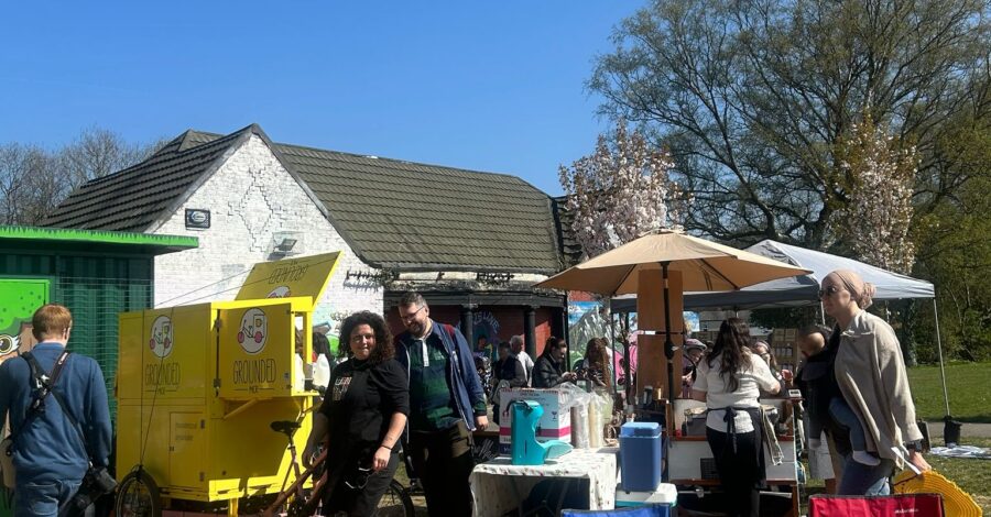 A small outdoor market with a few people bustling about. There are some parasols and also some chairs.