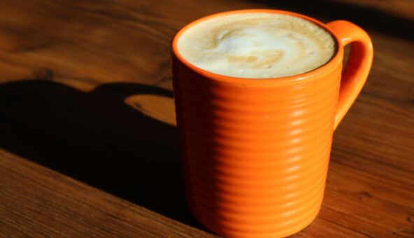 An orange mug full of coffee with a frothy, creamy white top.