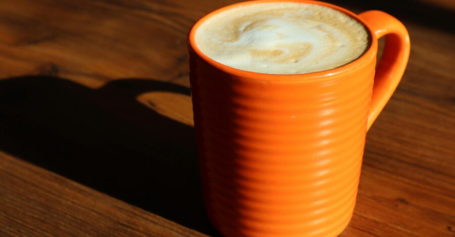 An orange mug full of coffee with a frothy, creamy white top.