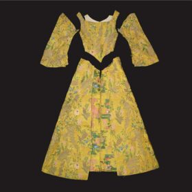 A yellow tudor-style long dress that has been unpicked. The skirt, the bodice and the arms are laid out separately on a flat surface.