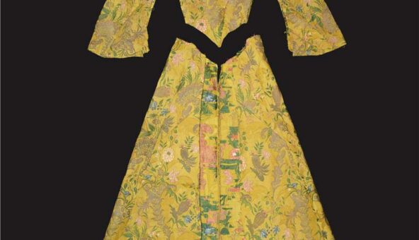 A yellow tudor-style long dress that has been unpicked. The skirt, the bodice and the arms are laid out separately on a flat surface.