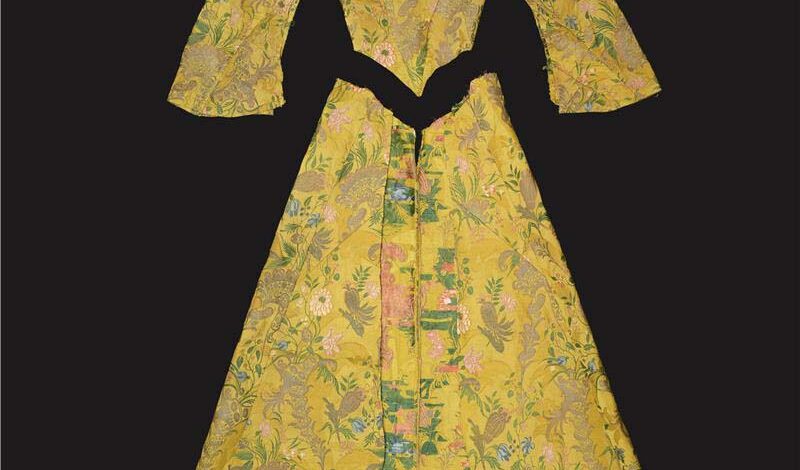 A yellow tudor-style long dress that has been unpicked. The skirt, the bodice and the arms are laid out separately on a flat surface.