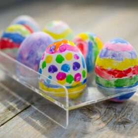 A clear plastic tray filled with six easter eggs that have been painted with bright colours and vivid patterns.