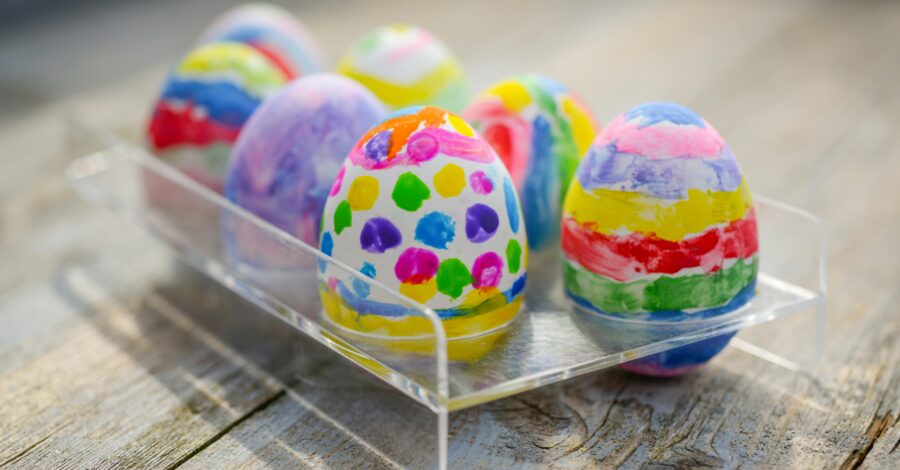 A clear plastic tray filled with six easter eggs that have been painted with bright colours and vivid patterns.