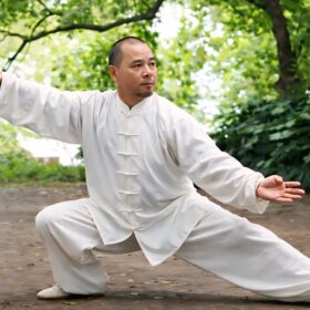 Man performing tai chi outside, in a white, traditional Chinese suit.