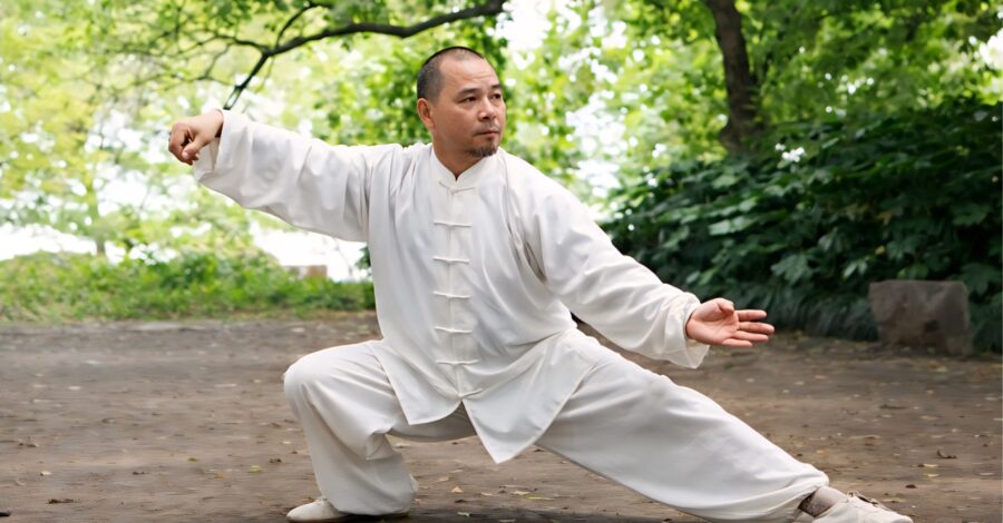Man performing tai chi outside, in a white, traditional Chinese suit.