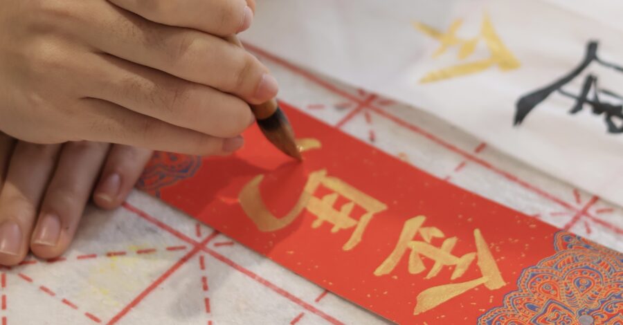 Close up of a hand writing Chinese Caligraphy, gold pen on a red paper.