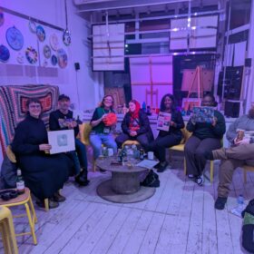 A group of artists sat inside OT creative space holding up artwork and smiling.