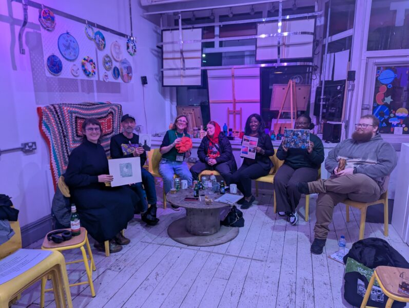 A group of artists sat inside OT creative space holding up artwork and smiling.