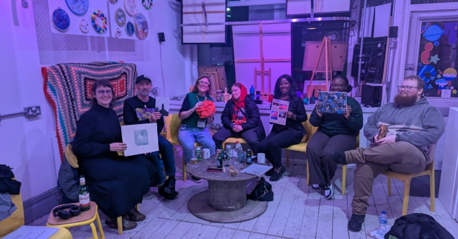 A group of artists sat inside OT creative space holding up artwork and smiling.