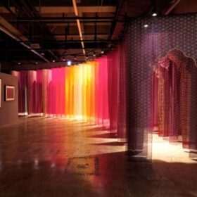 A succession of purple, yellow, orange fabrics creating a doorway that curves around a gallery space.
