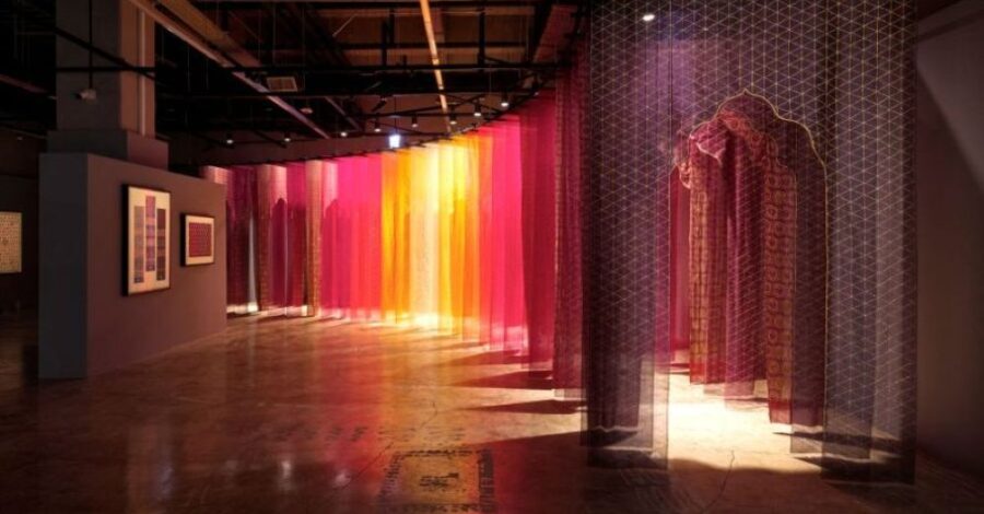 A succession of purple, yellow, orange fabrics creating a doorway that curves around a gallery space.