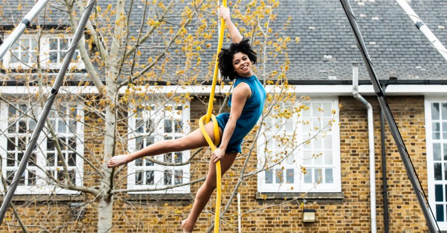 A circus performer wearing a turquoise costume performs off the ground on aerial ropes.