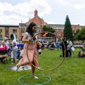 A performer holding a hula hoop in a grassy area. There are lots of people in the background.
