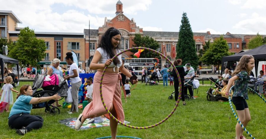 A performer holding a hula hoop in a grassy area. There are lots of people in the background.