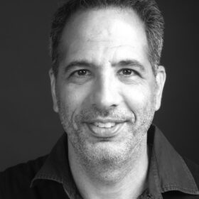 A black and white portrait photograph of Yotam Ottolenghi