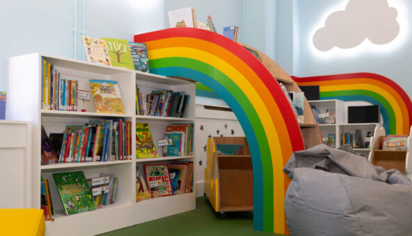 A room with white bookshelves filled with books and a rainbow structure in the centre of them.