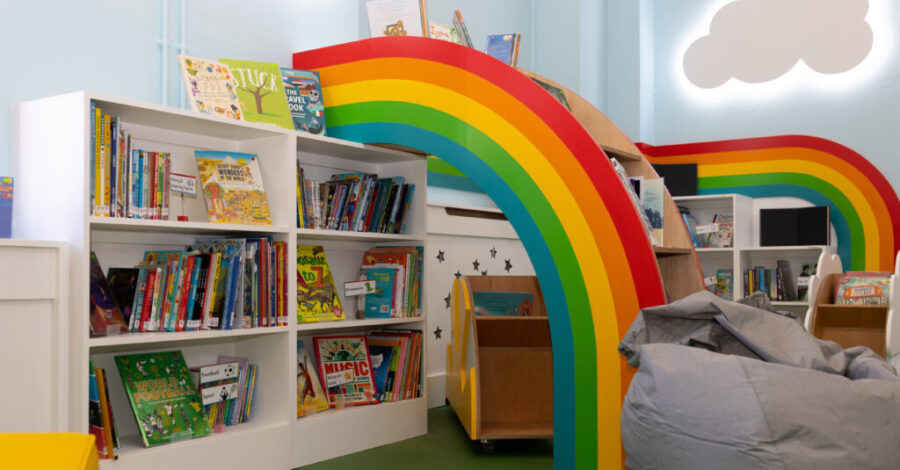A room with white bookshelves filled with books and a rainbow structure in the centre of them.